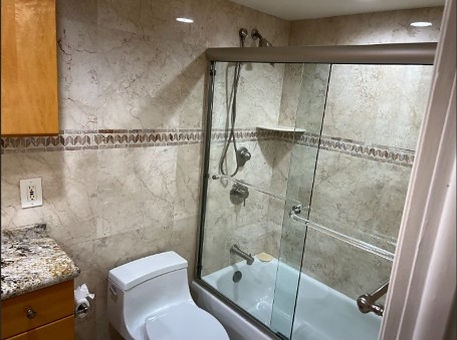 Condo bathroom featuring tile walls, glass shower enclosure, bathtub and granite vanity