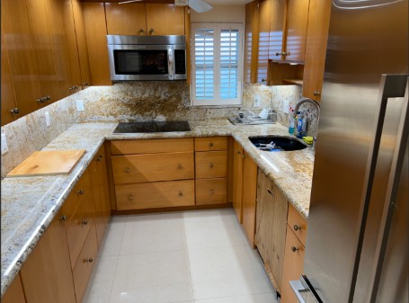 Condo kitchen with shining wood cabinets, granite counters and a stainless-steel refrigerator